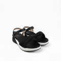 A pair of black wedge sandals with a thick braided rope detail across the instep and black ankle straps, shown on a white fabric backdrop.