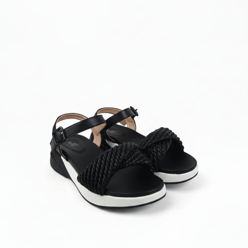 A pair of black wedge sandals with a thick braided rope detail across the instep and black ankle straps, shown on a white fabric backdrop.