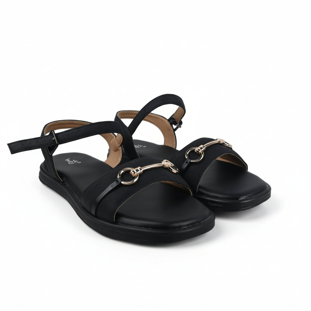 A pair of women's flat sandals in tan leather with double straps and gold-tone horsebit hardware, shown on a white studio backdrop with a shoebox partially visible.