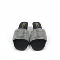 A pair of women's slide sandals with black feet and wide, textured metallic silver straps, shown next to their red and blue box on a white background.
