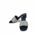A pair of women's heeled mule sandals with navy blue feet and silver glittery straps, shown on a white fabric backdrop with a red shoebox partially visible on the right.