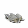 A pair of women's heeled slide sandals with textured silver woven straps and metallic silver block heels, shown on a white studio backdrop.