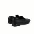 A pair of black leather penny loafers shown from a side-rear angle against a wrinkled white studio backdrop.