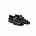 A pair of black leather loafers with a quilted chevron pattern on the sides, a smooth toe cap, and a gold-tone chain strap across the top, displayed on a light gray surface.