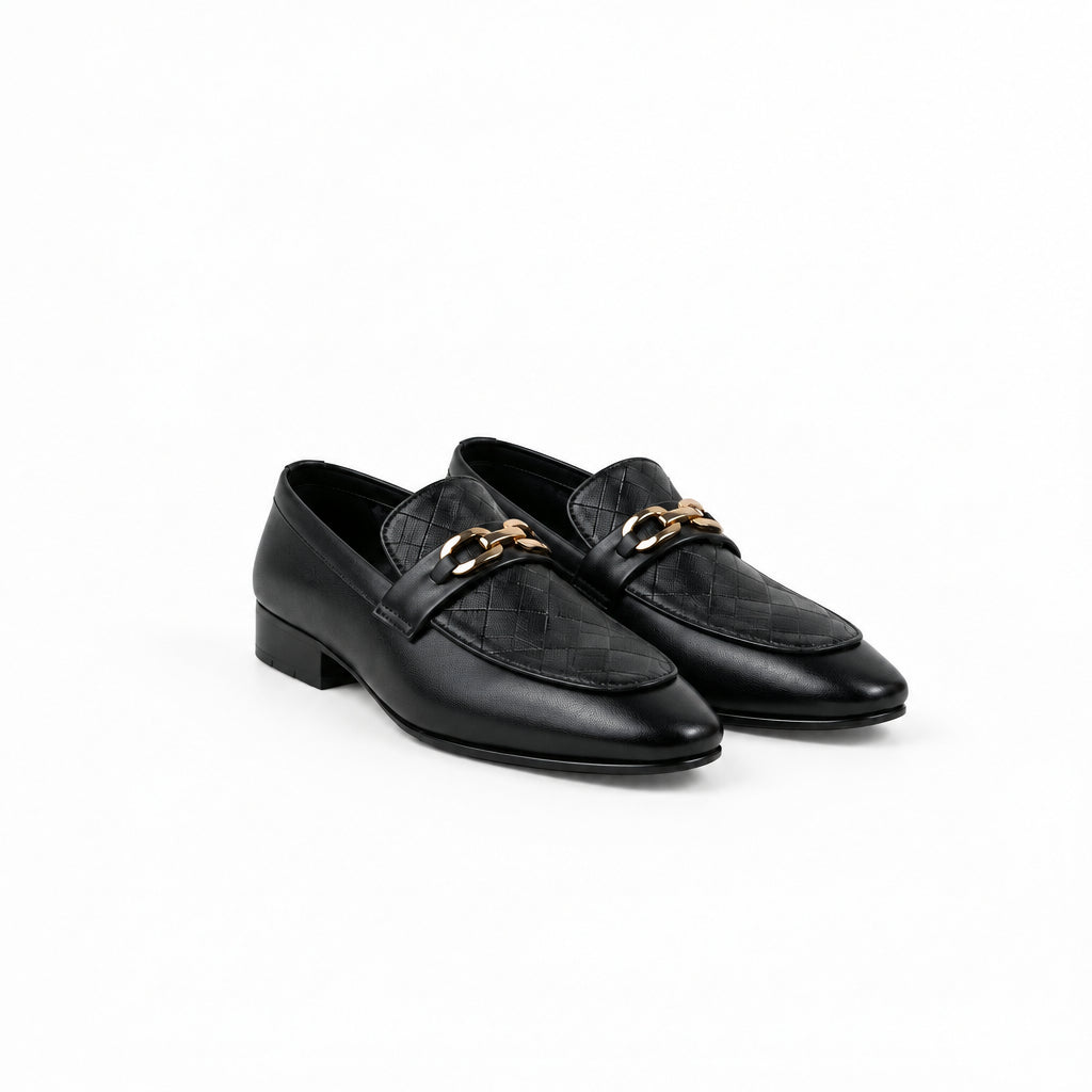A pair of black leather loafers with a quilted chevron pattern on the sides, a smooth toe cap, and a gold-tone chain strap across the top, displayed on a light gray surface.