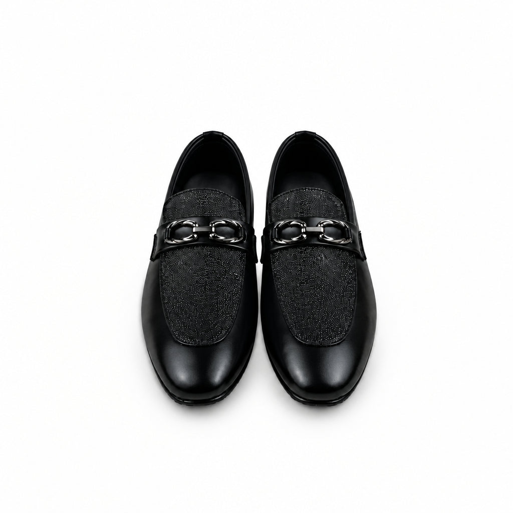A pair of black loafers with a textured fabric upper and a shiny black leather strap across the vamp, displayed on a white surface next to an orange shoebox.
