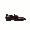A single dark brown leather loafer with a low block heel and a decorative strap detail across the vamp, shown from a side profile against a white fabric backdrop.
