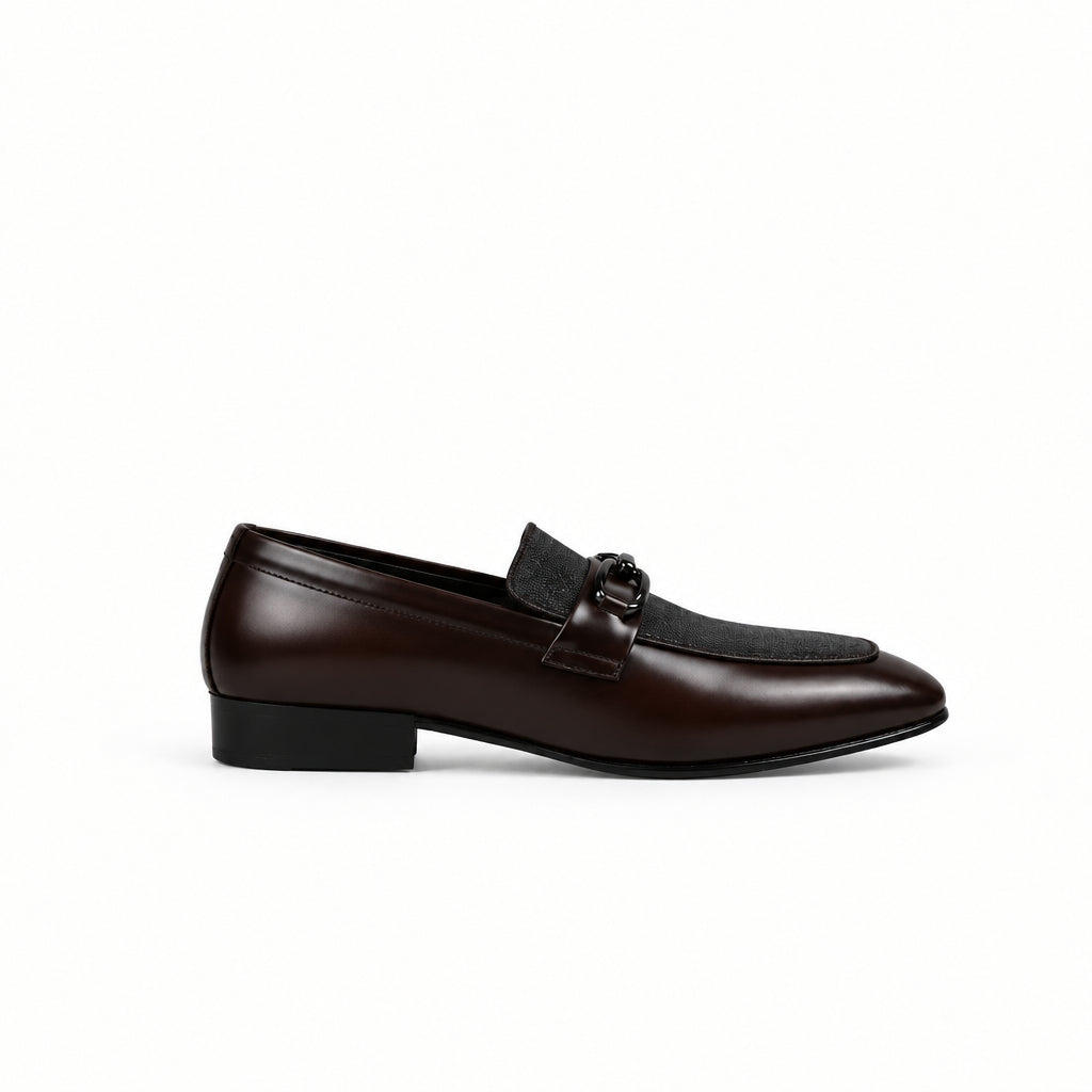 A single dark brown leather loafer with a low block heel and a decorative strap detail across the vamp, shown from a side profile against a white fabric backdrop.