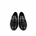 A pair of black leather loafers with a gold-tone horsebit detail across the vamp, displayed on a white fabric background next to an orange shoebox.