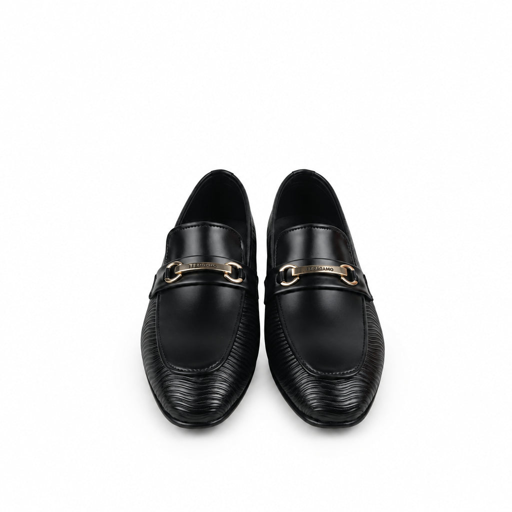 A pair of black leather loafers with a gold-tone horsebit detail across the vamp, displayed on a white fabric background next to an orange shoebox.