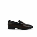 A single dark brown leather loafer with a textured pattern, low block heel, and a small gold-tone decorative accent on the strap, shown against a wrinkled white fabric background.