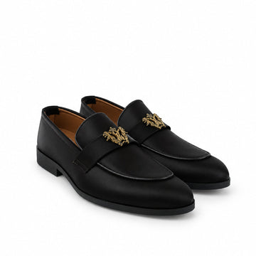 A pair of black leather penny loafers with gold-tone horsebit hardware, displayed on a white fabric backdrop.