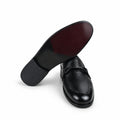 A pair of black leather penny loafers, with one shoe turned to show the dark reddish-brown underside of the sole against a plain white background.