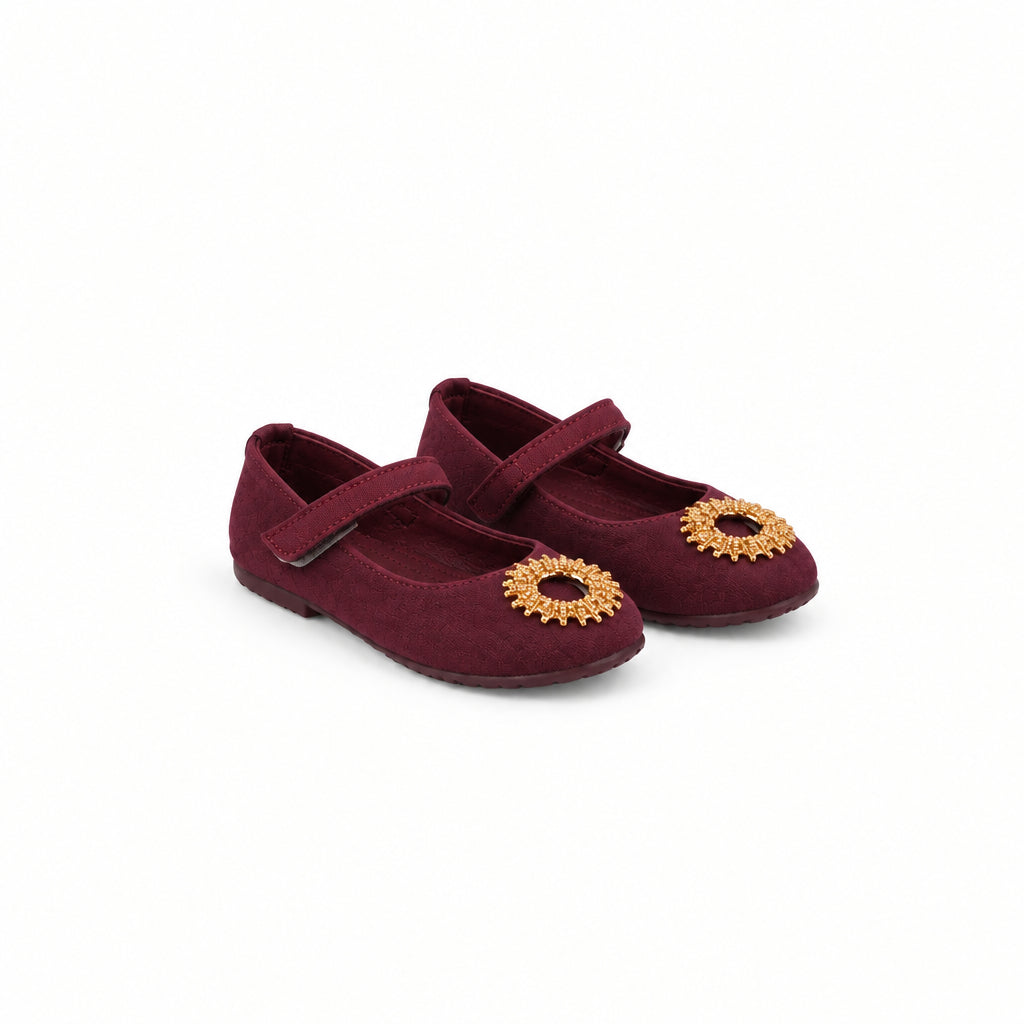 A pair of toddler's burgundy satin Mary Jane shoes with gold sunburst embellishments on the toes, shown against a plain white background.
