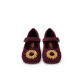A pair of dark burgundy ballet flats with gold circular floral embellishments on the toes, displayed on a white surface with a white backdrop.