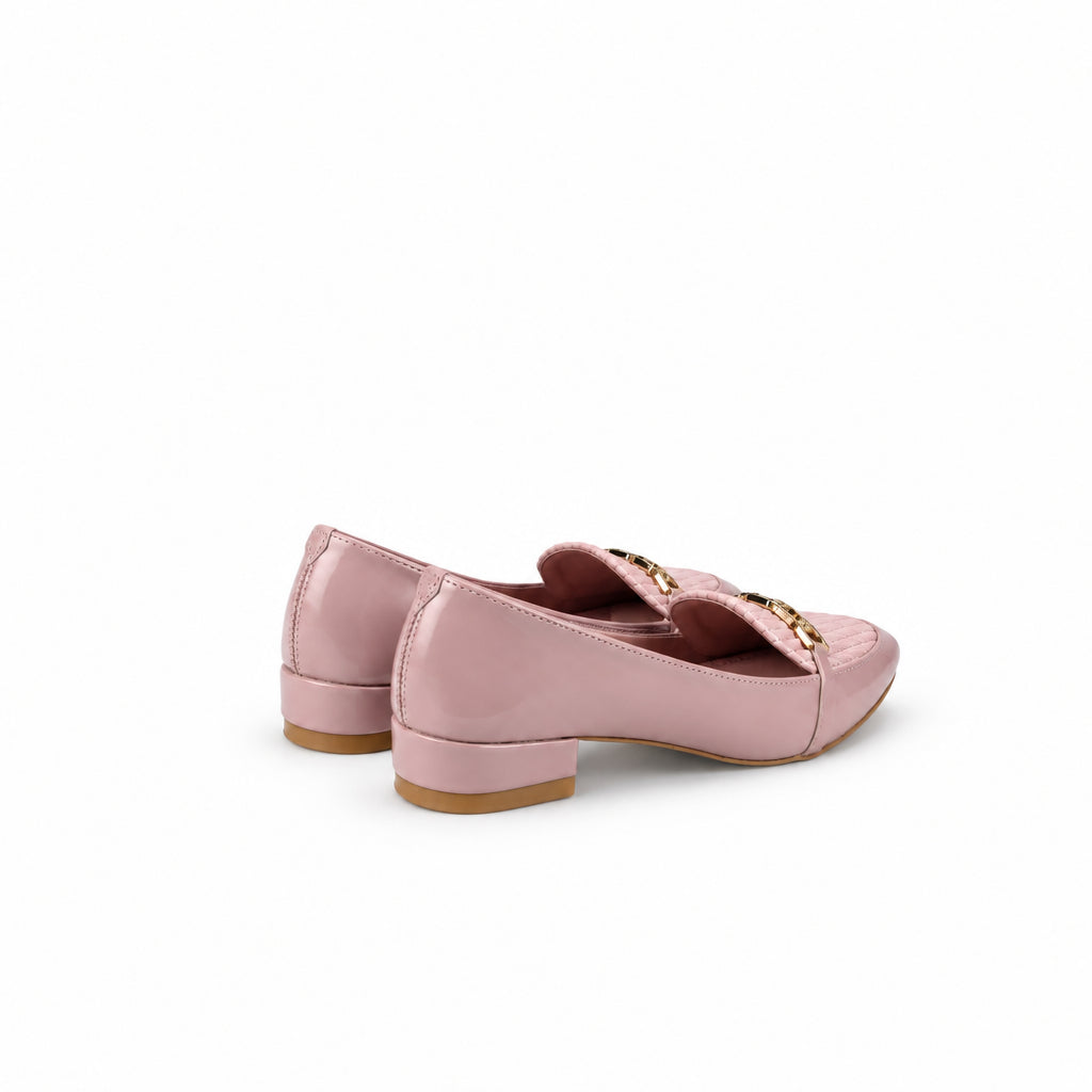 A pair of light pink patent leather loafers with a decorative bow featuring gold lettering, displayed on a white studio backdrop.