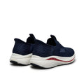 A pair of Skechers slip-on athletic sneakers in navy blue, featuring a textured knit upper, a thick white cushioned midsole, and a thin red accent stripe on the side.