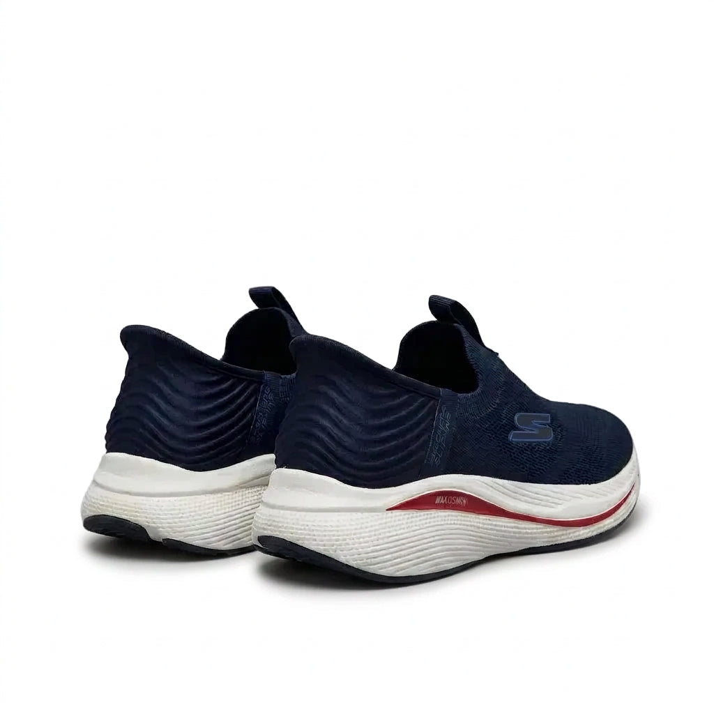 A pair of Skechers slip-on athletic sneakers in navy blue, featuring a textured knit upper, a thick white cushioned midsole, and a thin red accent stripe on the side.