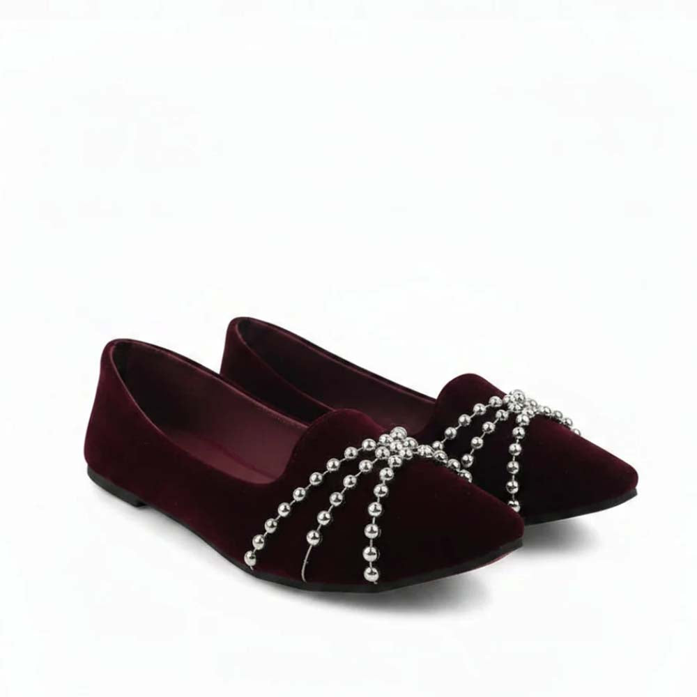 A pair of burgundy velvet flat shoes with silver beaded straps across the toes, shown on a clean white background.