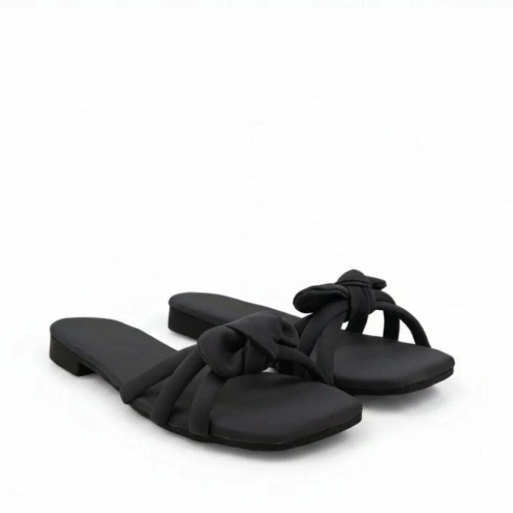A pair of black slide sandals with wide crisscross straps and a bow detail on the toe, set against a plain white background.