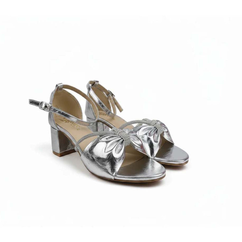 A pair of metallic silver strappy sandals with a block heel and bow detail on the toe, shown on a plain white background.
