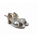 A pair of metallic silver strappy sandals with a block heel and bow detail on the toe, shown on a plain white background.